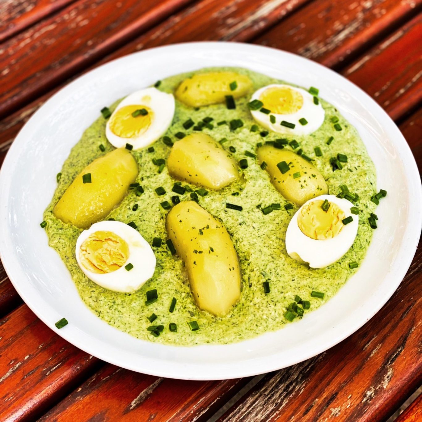 Ein Teller mit grüner Sauce, Kartoffeln und hartgekochten Eiern, garniert mit Schnittlauch.